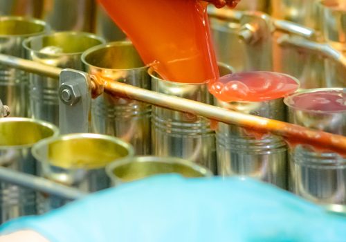 Canned fish factory. Food industry. Machine filling red tomato sauce into sardine can at food factory. Food processing production line. Food manufacturing industry. Cans of sardines on conveyor belt.
